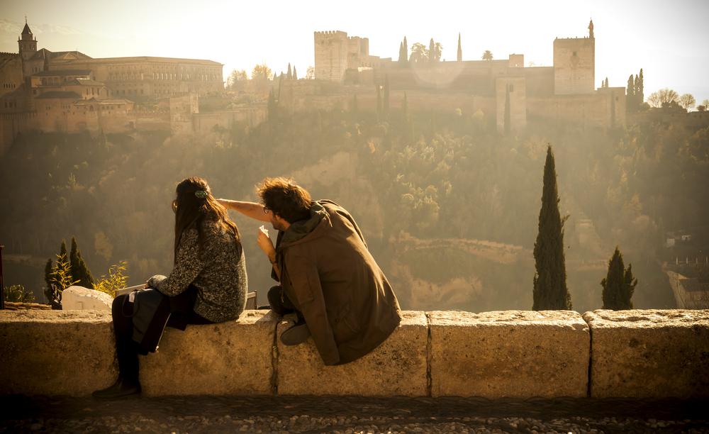 Couple sitting during sunset on a wall of the San Nicolás Viewpoint in Granada, Spain.